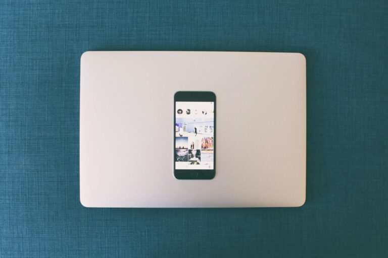 Flat lay of a smartphone on a laptop with social media photos on screen.